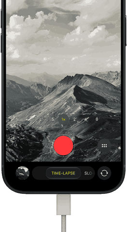 iPhone 18 Pro, Vorderseite, das Display zeigt eine Berglandschaft, mit der Kamera Modus Überlagerung im Zeitraffer Modus, mit dem Netzkabel am Ladeanschluss