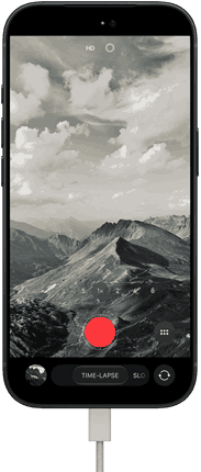 iPhone 18 Pro, Vorderseite, das Display zeigt eine Berglandschaft, mit der Kamera Modus Überlagerung im Zeitraffer Modus, mit dem Netzkabel am Ladeanschluss