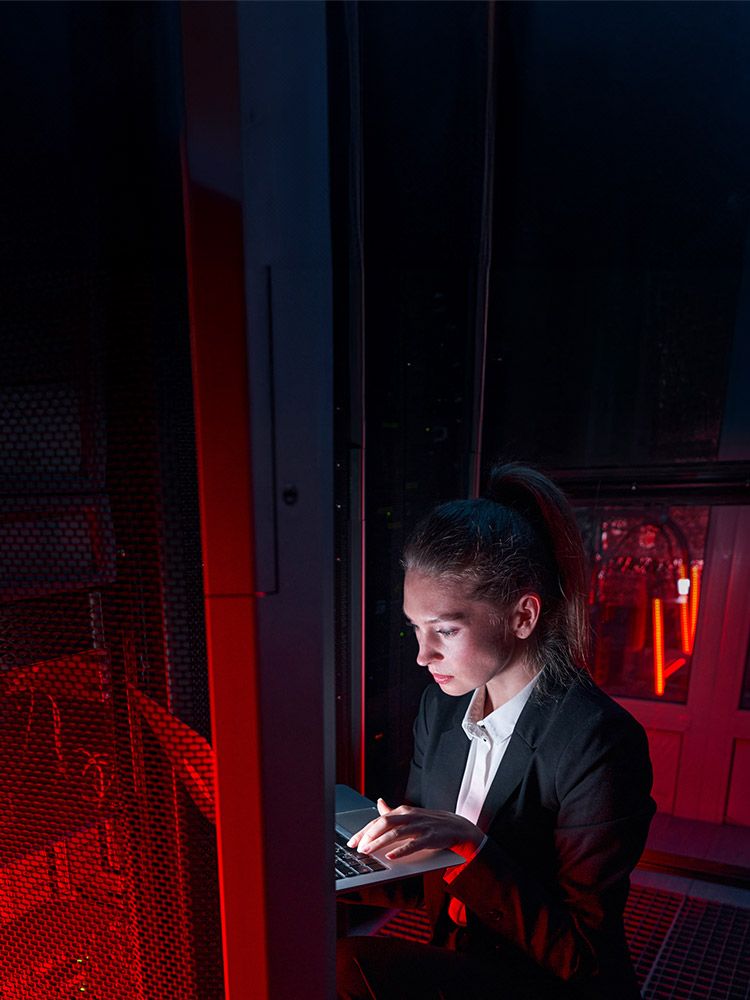 Digitale Souveräntiät: Frau mit Laptop arbeitet im Serverraum bei dunkler, roter Beleuchtung.